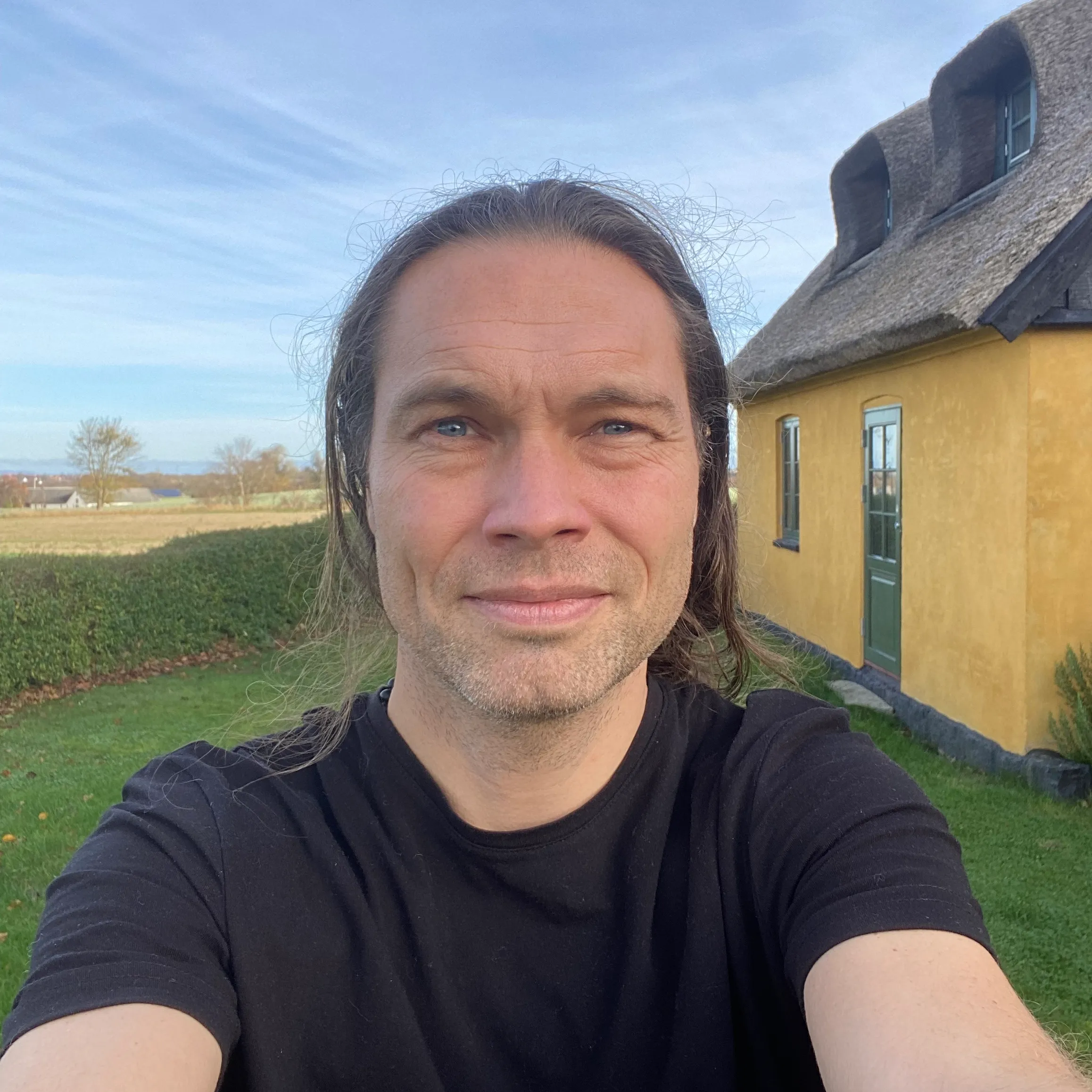 Benedict foran et gult, halmtækket hus